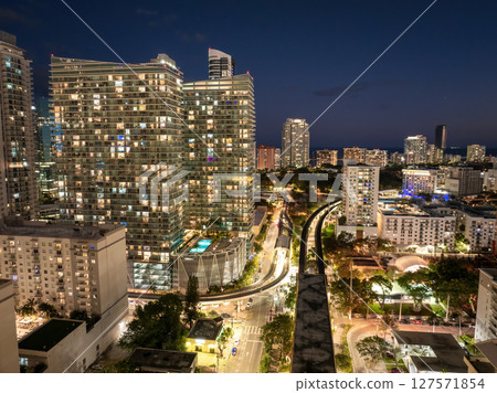Aerial view of public train tracks running through the modern downtown of Miami, Florida, USA. High-rise buildings over railroad at night 127571854