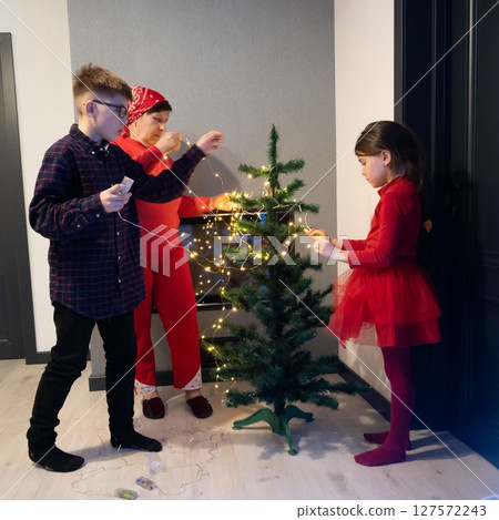 Family decorating a Christmas tree together, adding string lights and enjoying the festive season. 127572243