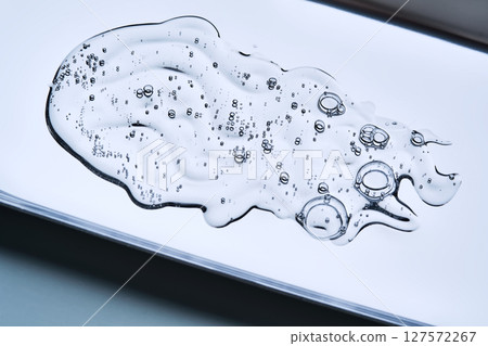 A beautiful drop of cosmetic product with bubbles on a blue background. A beautiful drop of cosmetic product with bubbles on a blue background. 127572267
