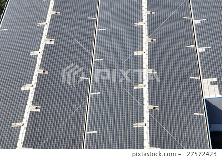 Aerial view of blue photovoltaic solar panels mounted on industrial building roof for producing green ecological electricity. Production of sustainable energy concept Aerial view of blue photovoltaic solar panels mounted on industrial building roof for producing green ecological electricity. Production of sustainable energy concept 127572423