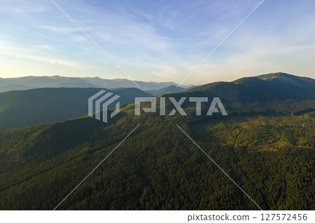 Aerial view of amazing scenery with dark mountain hills covered with forest pine trees at autumn sunrise. Beautiful wild woodland at dawn Aerial view of amazing scenery with dark mountain hills covered with forest pine trees at autumn sunrise. Beautiful wild woodland at dawn 127572456