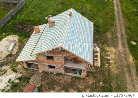 Aerial view of a brick house with wooden roof frame under construction. 127572464