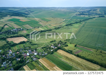 Aerial landscape view of village houses and distant green cultivated agricultural fields with growing crops on bright summer day 127572475