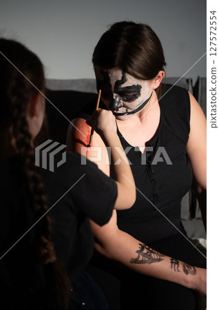 A young girl carefully paints a spooky skull design onto her mother's arm for Halloween. A young girl carefully paints a spooky skull design onto her mother's arm for Halloween. 127572554