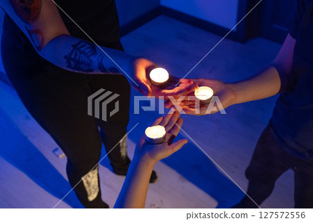 Three individuals hold small candles, creating a serene and mystical atmosphere in a dimly lit room. 127572556