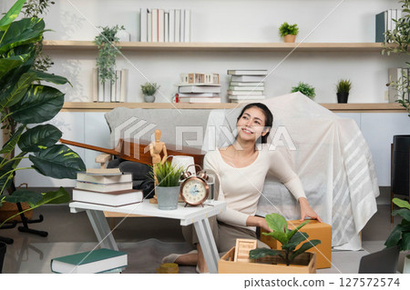 Moving and Organizing. Woman joyfully unpacking boxes in a cozy indoor space. Moving and Organizing. Woman joyfully unpacking boxes in a cozy indoor space. 127572574