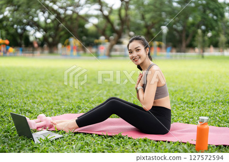 Yoga and Positive Vibes. Young woman practicing yoga stretches outdoors with a laptop in a park. 127572594