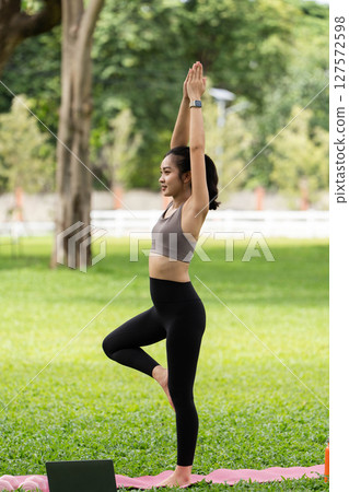 Yoga and balance. Young woman practicing tree pose outdoors in a green park. Yoga and balance. Young woman practicing tree pose outdoors in a green park. 127572598
