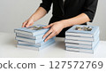 Woman in black clothes arranging hardcover photo books on a white desk in a minimal interior 127572769