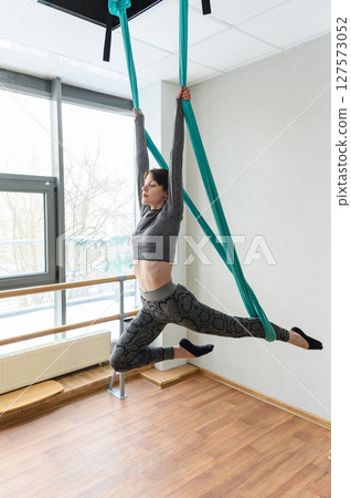 Woman performing aerial silks acrobatics in bright dance studio. Woman performing aerial silks acrobatics in bright dance studio. 127573052
