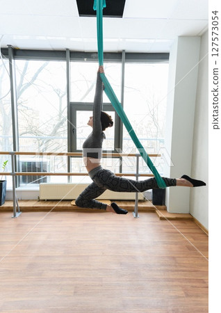 Woman performing aerial silks acrobatics in bright dance studio. Woman performing aerial silks acrobatics in bright dance studio. 127573054