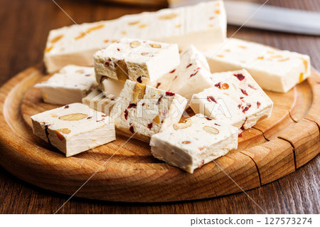White nougat bars with almonds and dried fruit on cutting board on wooden table. White nougat bars with almonds and dried fruit on cutting board on wooden table. 127573274