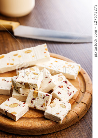 White nougat bars with almonds and dried fruit on cutting board on wooden table. White nougat bars with almonds and dried fruit on cutting board on wooden table. 127573275