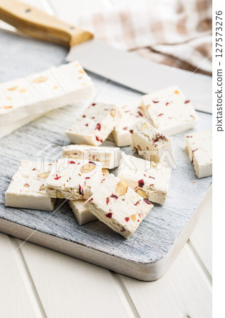 White nougat bars with almonds and dried fruit on cutting board on white table. White nougat bars with almonds and dried fruit on cutting board on white table. 127573276