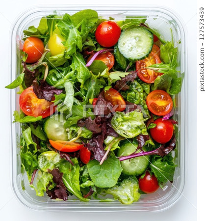 A fresh mixed greens salad, packaged in a clear plastic container. Includes crisp lettuce, juicy cherry tomatoes, and refreshing cucumber slices. A quick and nutritious meal for healthy lifestyle 127573439