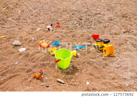 Children beach toys scattered on sand near the shoreline. Childhood, summer vacation and carefree playtime by the sea. 127573692