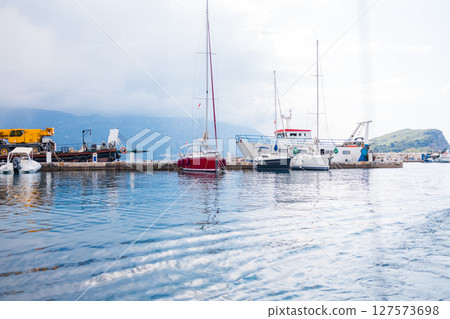 Boats docked at harbor under cloudy sky with construction vehicle on pier. Marina transport, nautical lifestyle and industrial elements by the sea. Boats docked at harbor under cloudy sky with construction vehicle on pier. Marina transport, nautical lifestyle and industrial elements by the sea. 127573698