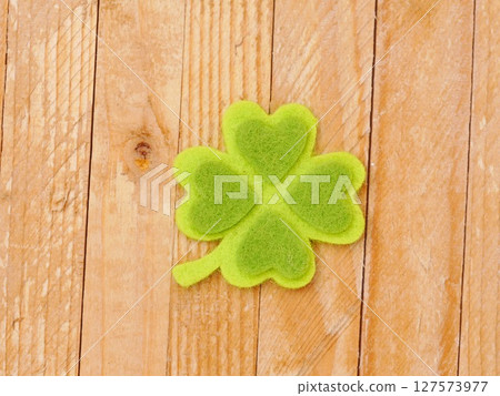 A green shamrock with four hearts on it sits on a wooden surface A green shamrock with four hearts on it sits on a wooden surface 127573977