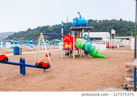 Colorful children playground on a sandy beach near the sea. Vacation concept, family tourism and beachside leisure activities for kids. 127575375