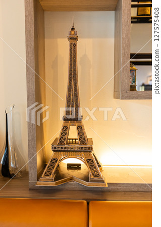 Miniature Eiffel Tower model placed on a wooden shelf. Parisian elegance, European landmarks and interior design inspired by French cultural heritage. Miniature Eiffel Tower model placed on a wooden shelf. Parisian elegance, European landmarks and interior design inspired by French cultural heritage. 127575408