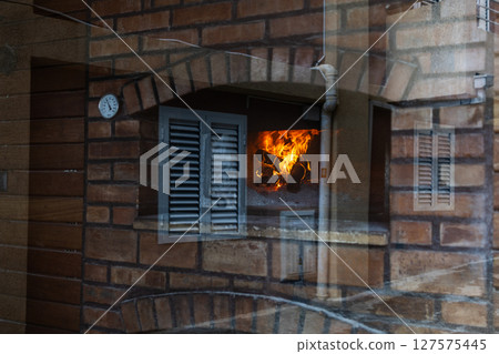 Fireplace glow seen through reflective window. Urban texture layers and warm flame create an abstract blend of home and environment. 127575445