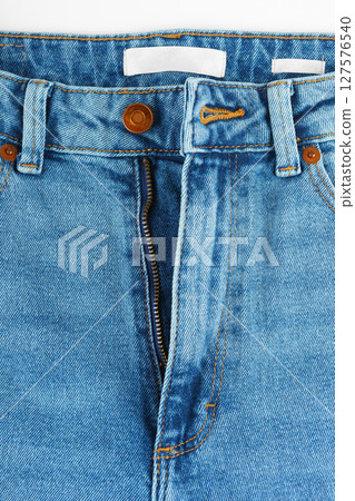 Front side of blue jeans pants. Design details, metal button, waistband and opened zipper close up 127576540