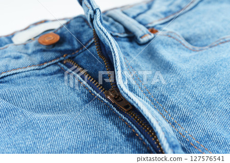 Close-up of denim jeans button and zipper, detailed view of textile, stitching, and copper hardware 127576541