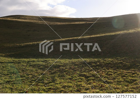 A hillside with a grassy field and a cloudy sky A hillside with a grassy field and a cloudy sky 127577152