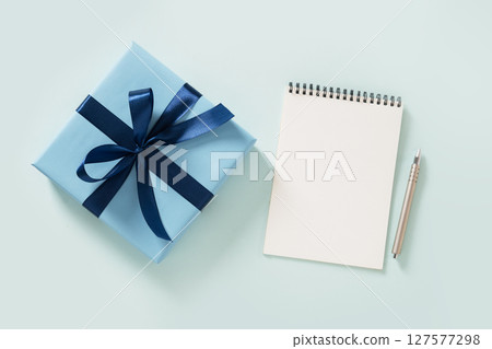 Blue gift box, white blank, spiral notebook and pen on pastel blue background. Invitation. Flat lay. View from above. Copy space. 127577298