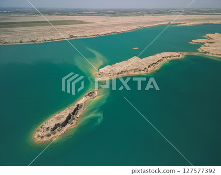 Sandy desert meeting waters of Kuimazar Reservoir with distant fields visible 127577392