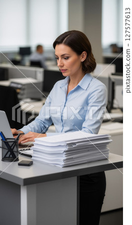 Female clerk stacks documents in a busy office. 127577613