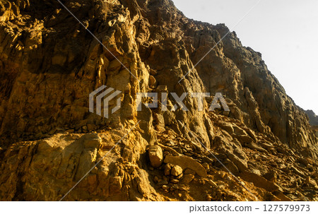Close-up of steep vertical desert cliffs in Egypt, with rugged textures and golden tones under strong sun Close-up of steep vertical desert cliffs in Egypt, with rugged textures and golden tones under strong sun 127579973