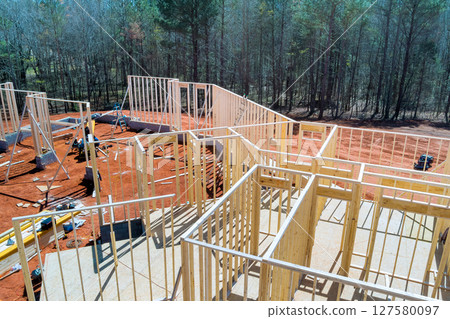 Workers are constructing beams frame of new house surrounded by trees on suburban location landscape 127580097