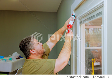 Man works diligently to caulk window frame in home renovation project, his handyman skills. 127580107