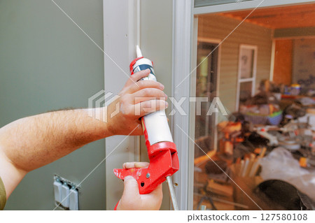 Applying caulk carefully to seal gaps around window for better insulation aesthetics. Applying caulk carefully to seal gaps around window for better insulation aesthetics. 127580108