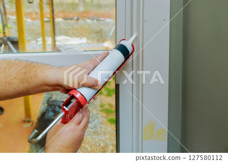 Hands apply sealant to window frame in home improvement setting during works day, precise work. Hands apply sealant to window frame in home improvement setting during works day, precise work. 127580112