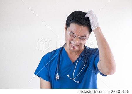 An Asian male nurse or doctor in blue scrubs and gloves showing signs of frustration and stress An Asian male nurse or doctor in blue scrubs and gloves showing signs of frustration and stress 127581926