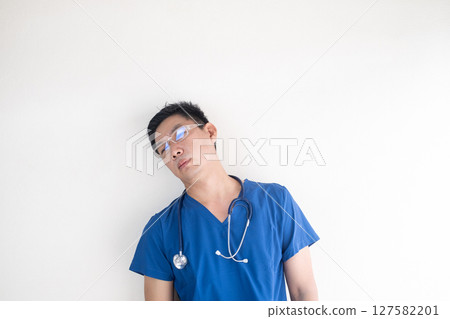 Exhausted Male Nurse Leaning Against Wall in Scrubs Exhausted Male Nurse Leaning Against Wall in Scrubs 127582201