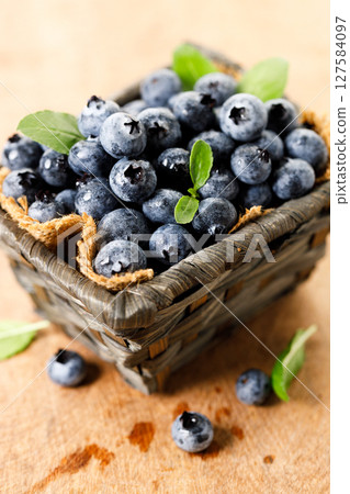 Ripe blueberries in wicker basket on wooden table. 127584097