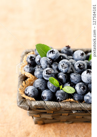 Ripe blueberries in wicker basket on wooden table. 127584101