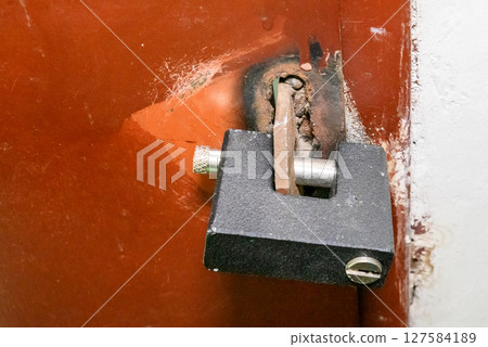 orange old iron door to house with black padlock 127584189