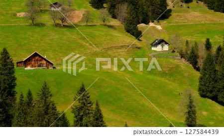 Scenic view of green hills and traditional houses under clear skies during daytime in a tranquil alpine landscape Scenic view of green hills and traditional houses under clear skies during daytime in a tranquil alpine landscape 127584439