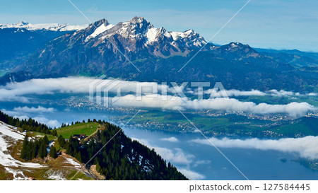 Mountains and clouds above lake with small village nestled in green valley on a clear spring day 127584445