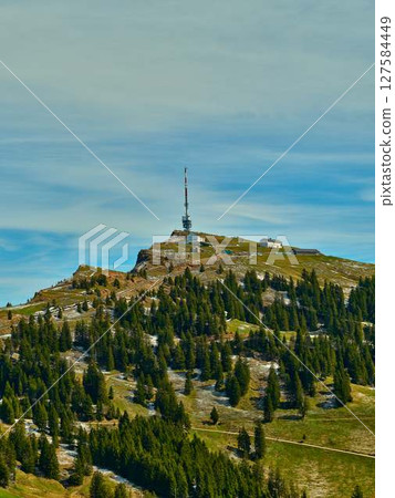 Mountaintop landscape features communication tower surrounded by lush green forest under a clear sky 127584449