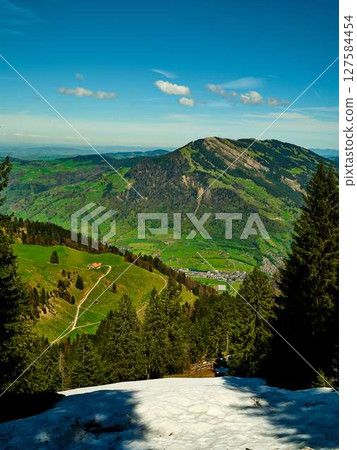 Scenic view from a mountain peak showcasing lush green valleys and distant hills on a bright sunny day 127584454