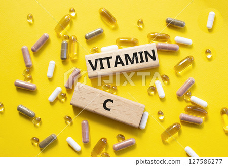 Vitamin C symbol. Concept word Vitamin C on wooden blocks. Beautiful yellow background with pills. Medicine and Vitamin C concept. Copy space 127586277