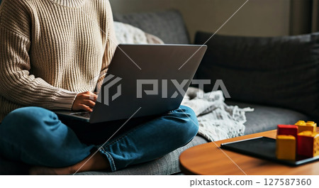 Modern young mother working from home on laptop surrounded by baby items 127587360