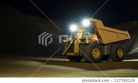 yellow dump truck on road construction site at night with bright headlights, construction concept 127588129