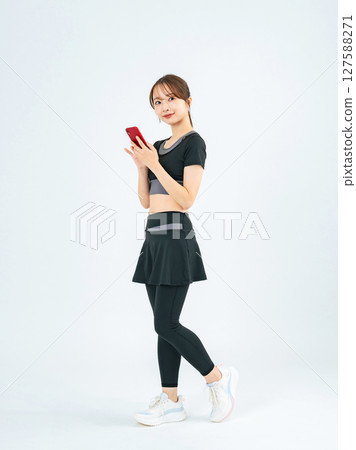 Full-body photo of a woman wearing sportswear and looking at her smartphone Full-body photo of a woman wearing sportswear and looking at her smartphone 127588271