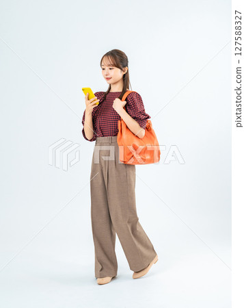 Full-body photo of a woman in casual wear walking with a smartphone Full-body photo of a woman in casual wear walking with a smartphone 127588327